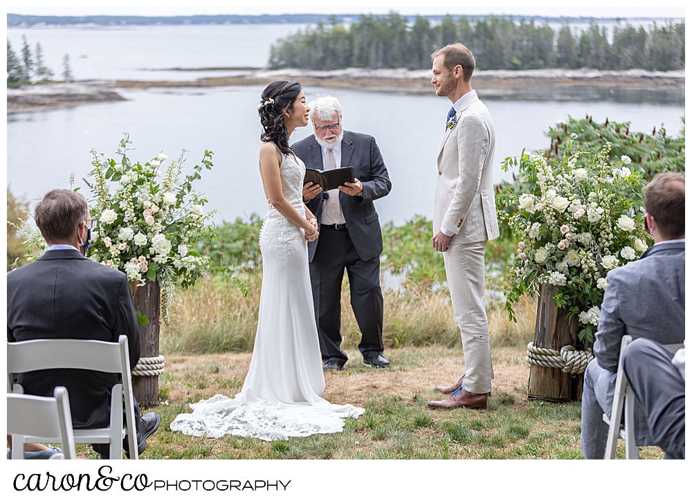 brideand groom stand in front of their officiant, on the lawn of their Grey Havens Inn wedding ceremony, Georgetown Maine