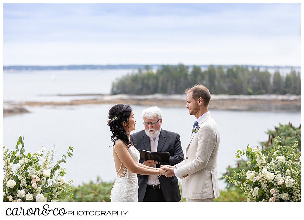 bride and groom holding hands in front of the officiant for their Grey Havens Inn wedding ceremony, Georgetown Maine