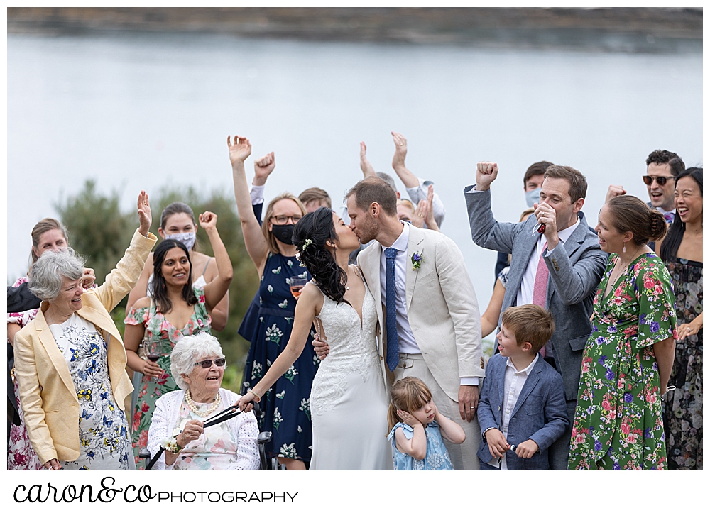 bride and groom, surrounded by their guests, kiss on the lawn at their Grey Havens Inn wedding, Georgetown Maine