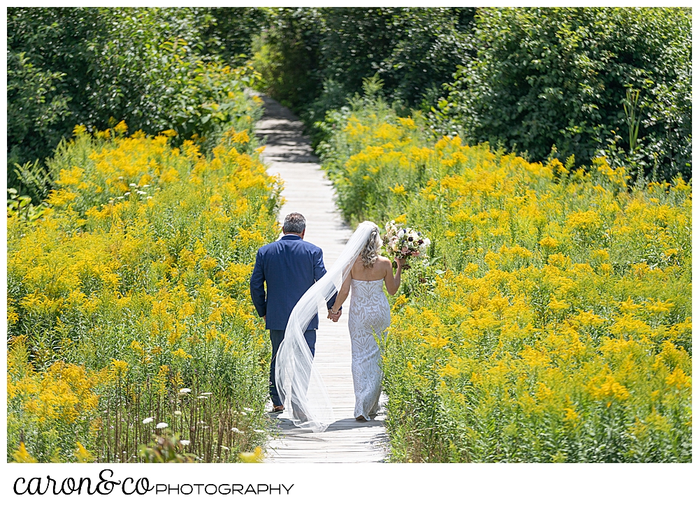 bride and groom walking down a boardwalk, amid yellow flowers