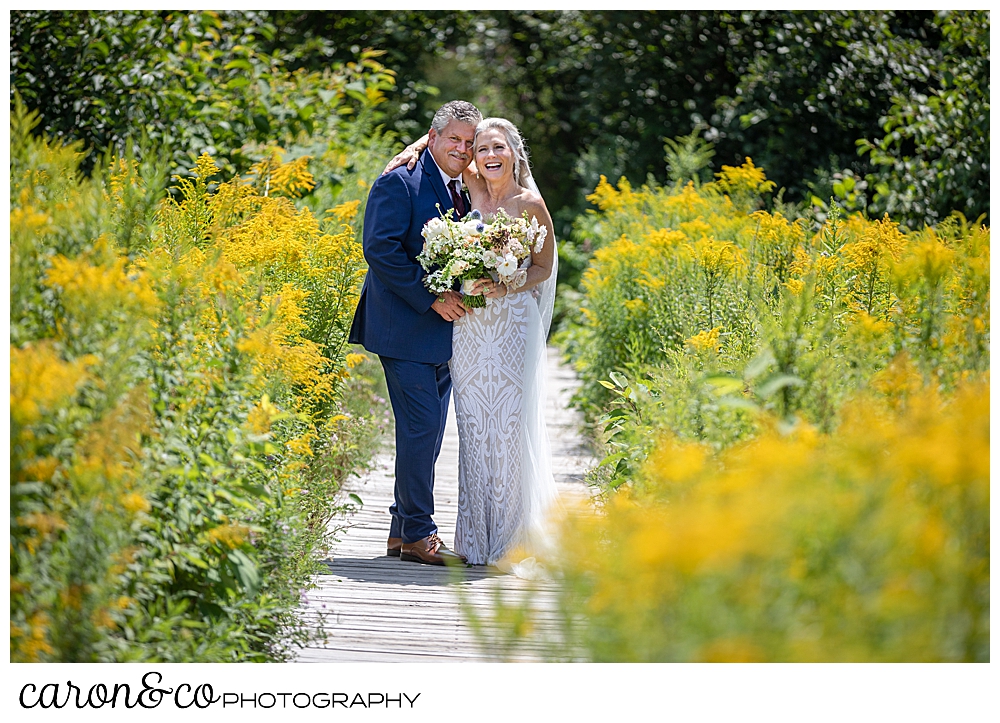 bride and groom posing on a boardwalk amid yellow flowers