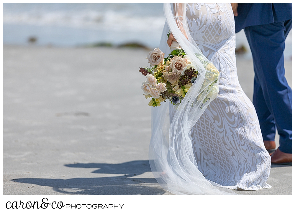 bride and groom walking along the water at the beach, the brides bouquet hangs down