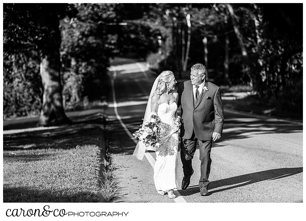 black and white photo of a bride and groom walking along the side of the road