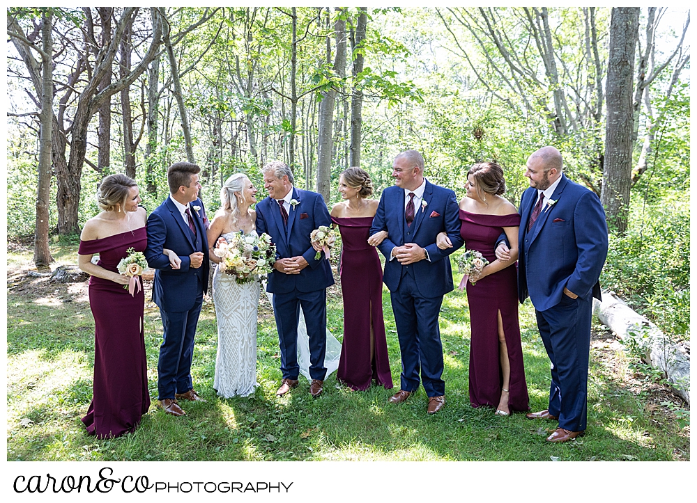 bride and groom with their bridal party in the woods, linking arms and walking
