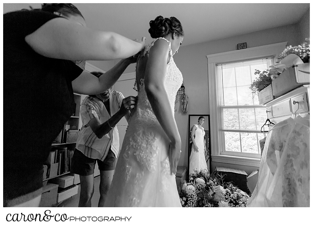 sweet summertime wedding, black and white photo of bride getting into her wedding dress with her mother and matron of honor