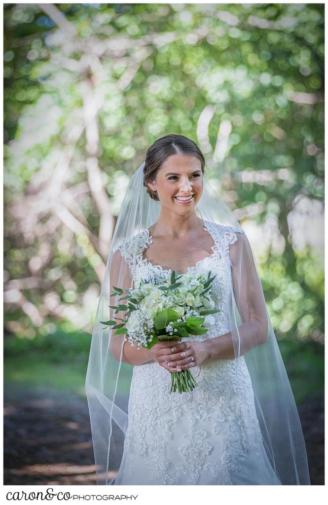 bride in a white wedding dress and veil, holding a green and white bouquet, smiling as the groom walks towards her