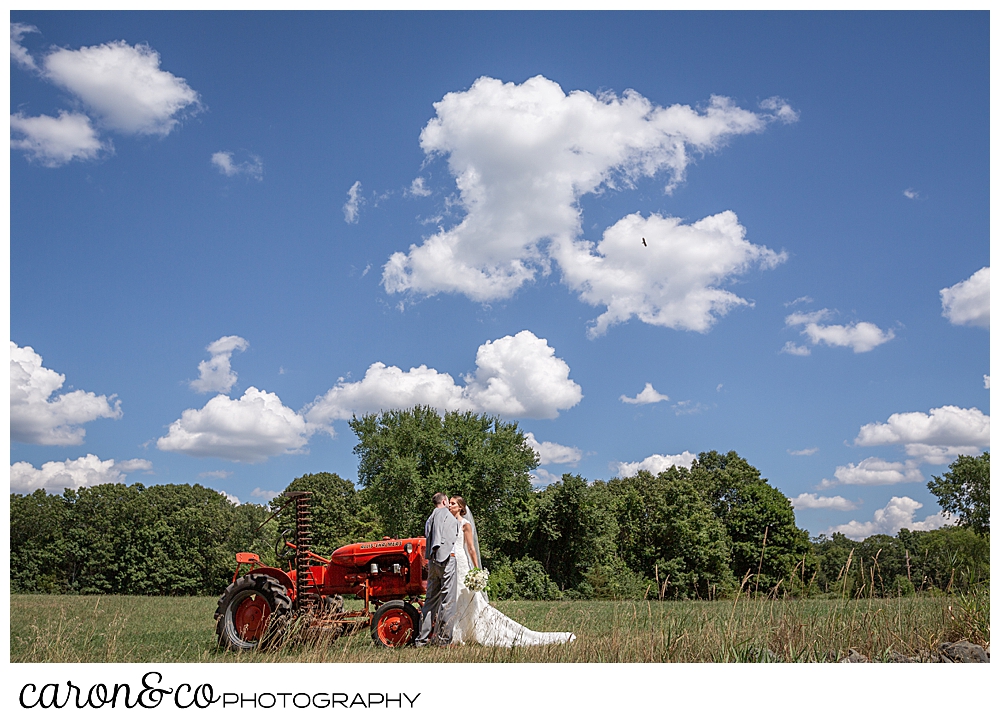 sweet summertime wedding day in rhode island, bride and groom kissing next to an orange tractor in a field