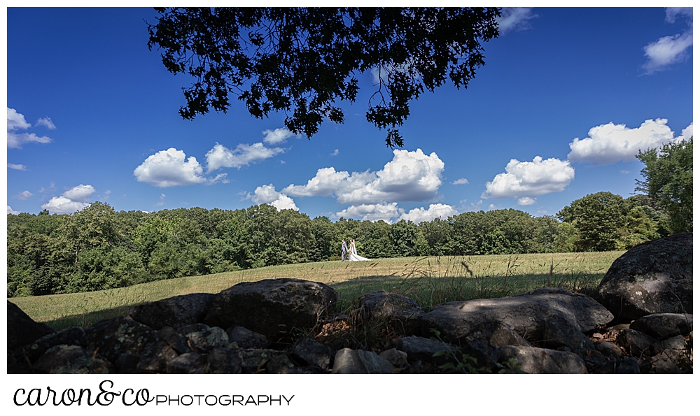 sweet summertime wedding with bride and groom walking hand in hand in a field