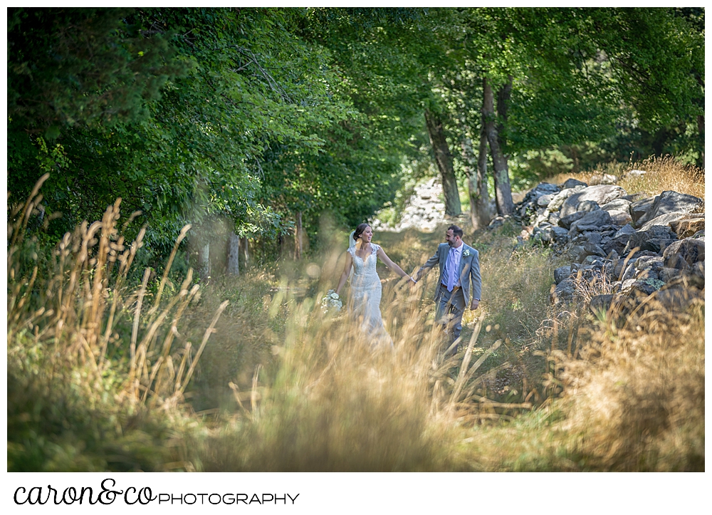 sweet summertime wedding day bride and groom walk hand in hand in a field