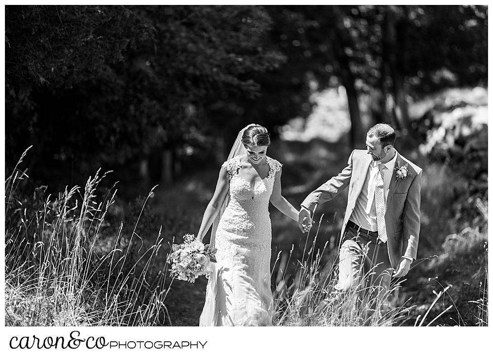 sweet summertime wedding in rhode island, black and white photo of bride and groom walking and holding hands in a grassy field