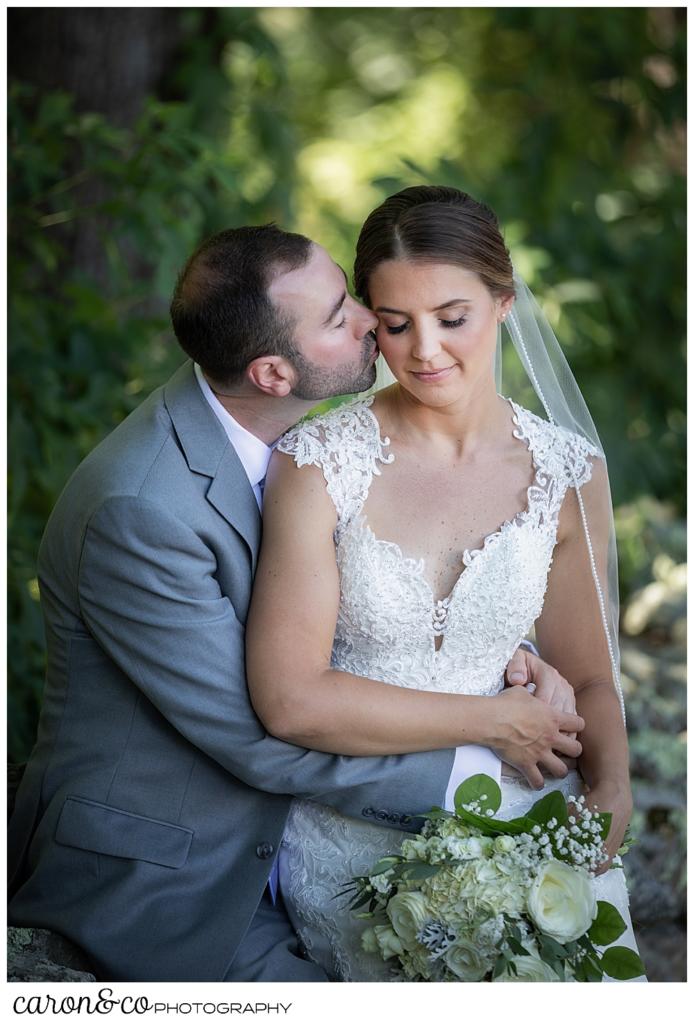 sweet summertime wedding photo with bride sitting on the groom's lap, while he kisses her cheek