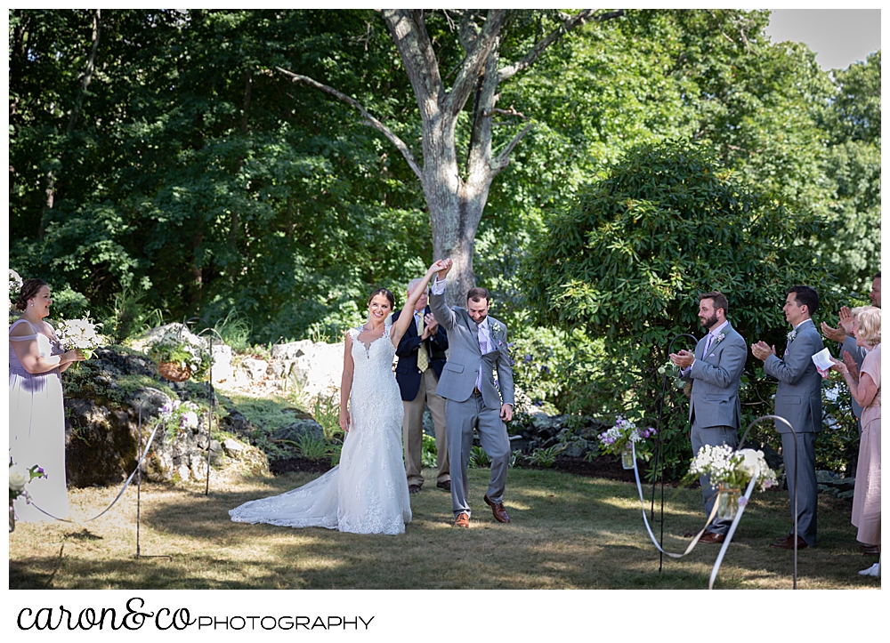 sweet summertime wedding ceremony photo of the bride and groom facing their guests, hands clasped, arms raised