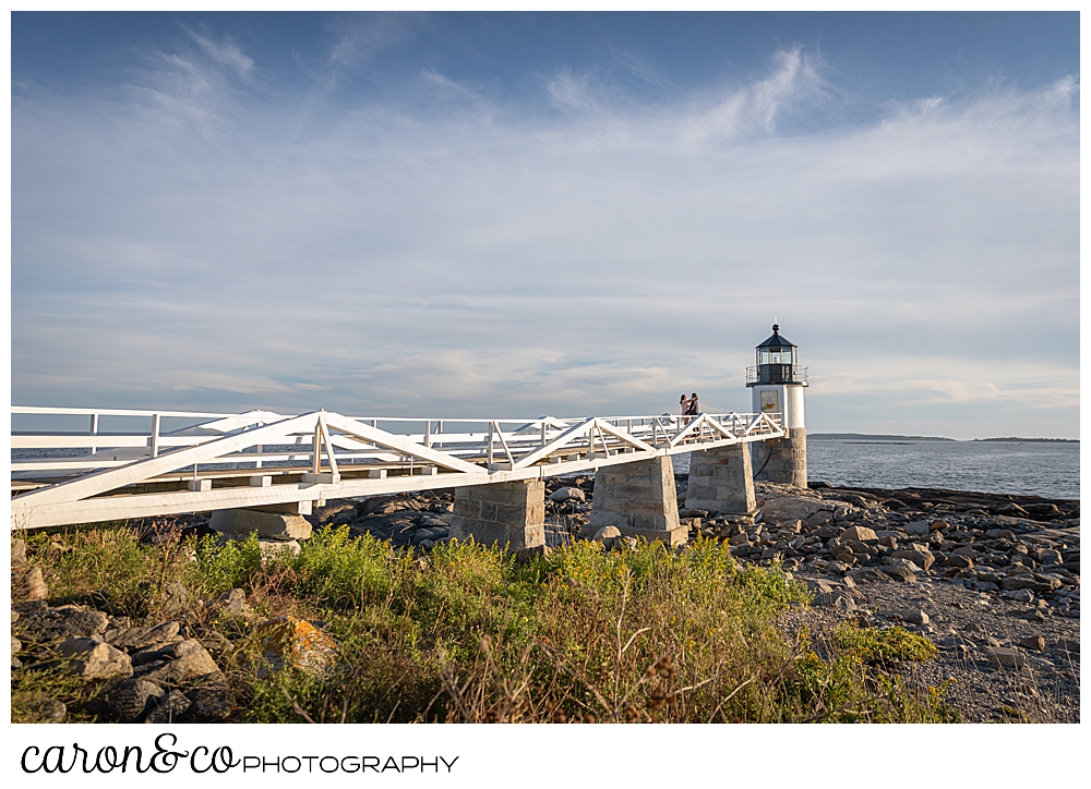 a woman and man are walking toward Marshall Point Lighthouse during their Port Clyde Maine engagement photo session