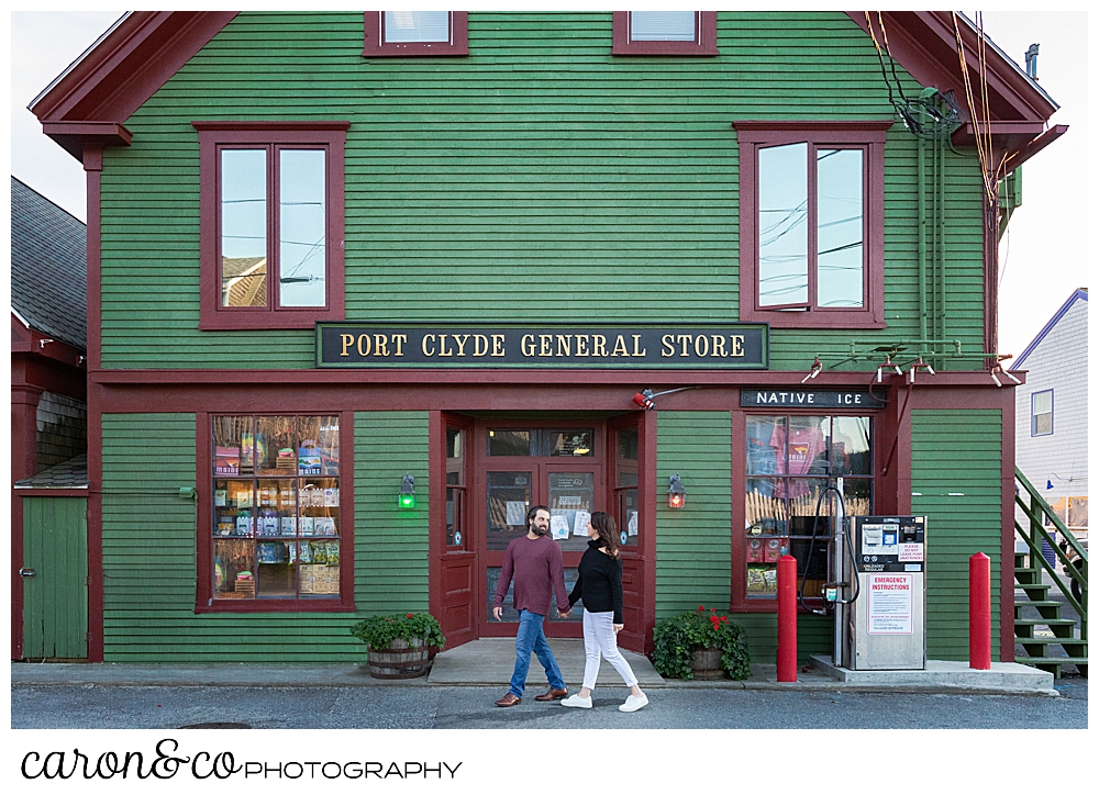 A man and woman are walking hand in hand past the Port Clyde General Store, during their Port Clyde Maine engagement