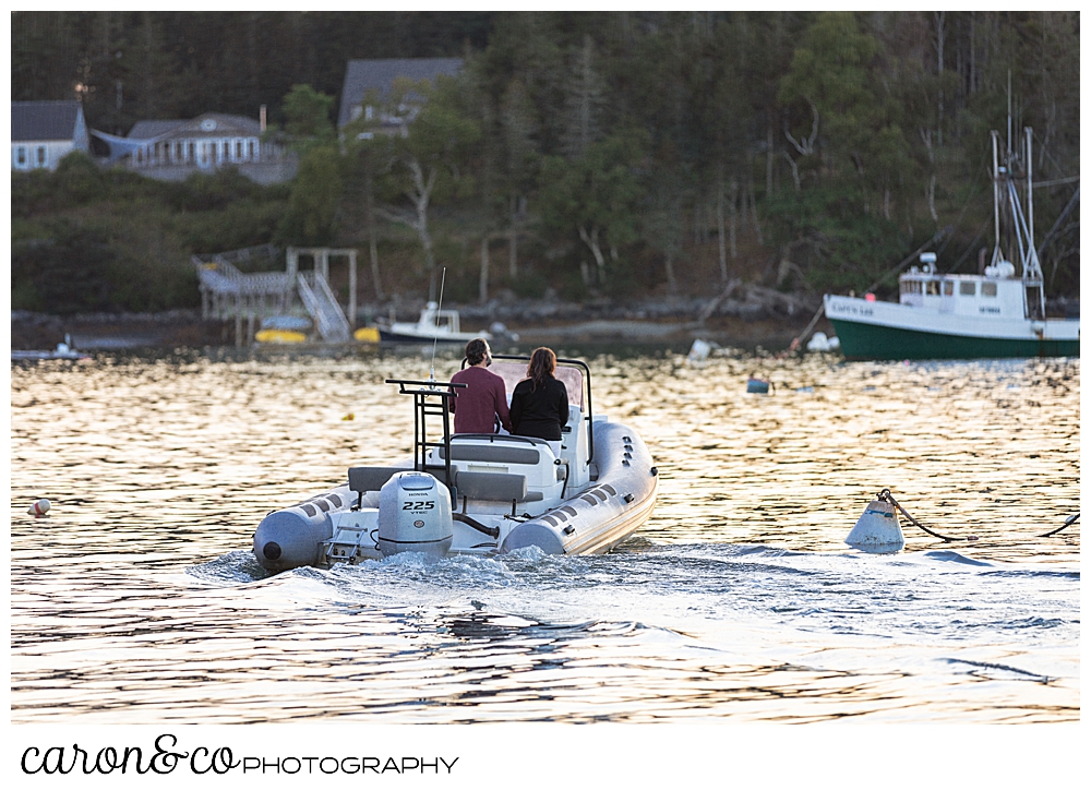 a man and a woman with their backs to the camera, are moving away in a brig inflatable boat, during their Port Clyde engagement photos