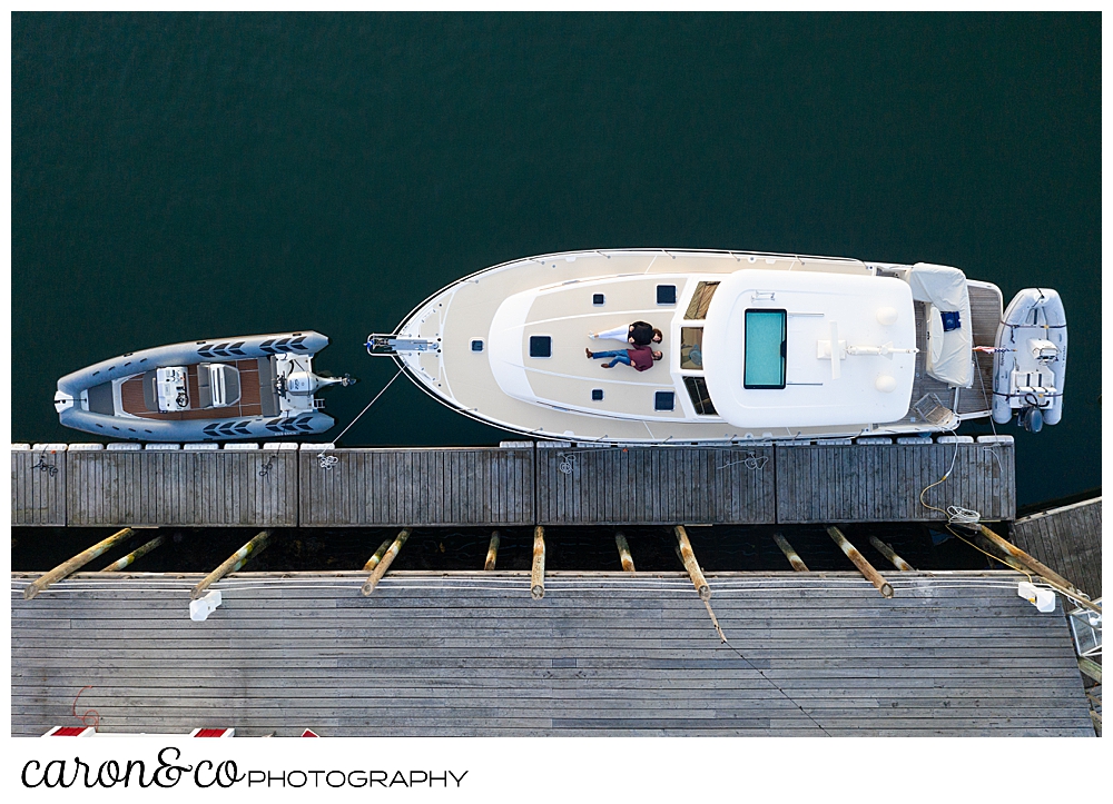 a couple are lying on the bow of a Sabre sailboat, during their Port Clyde Maine engagement