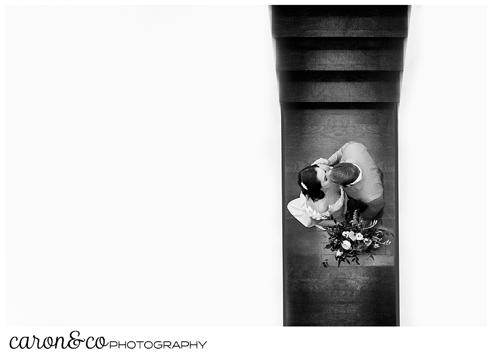 black and white photo of a bride and groom kissing at the bottom of the stairway at their Portland Press Hotel wedding