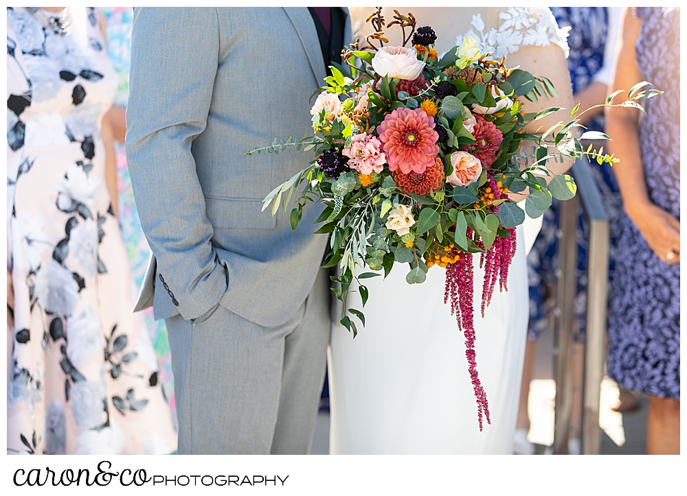 a bride and groom stand together among their guests, the bride's bouquet is the subject of the photo, flowers by Harmon's Floral Company