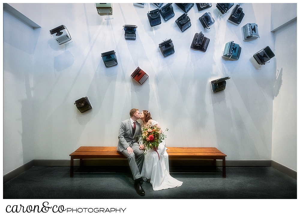 a bride and groom kiss underneath a wall of vintage typewriters at the Press Hotel Portland Maine