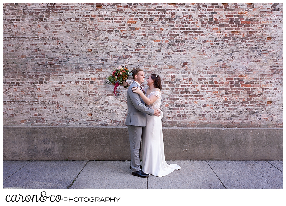 a bride and groom slow dance in front of a brick wall in Portland Maine