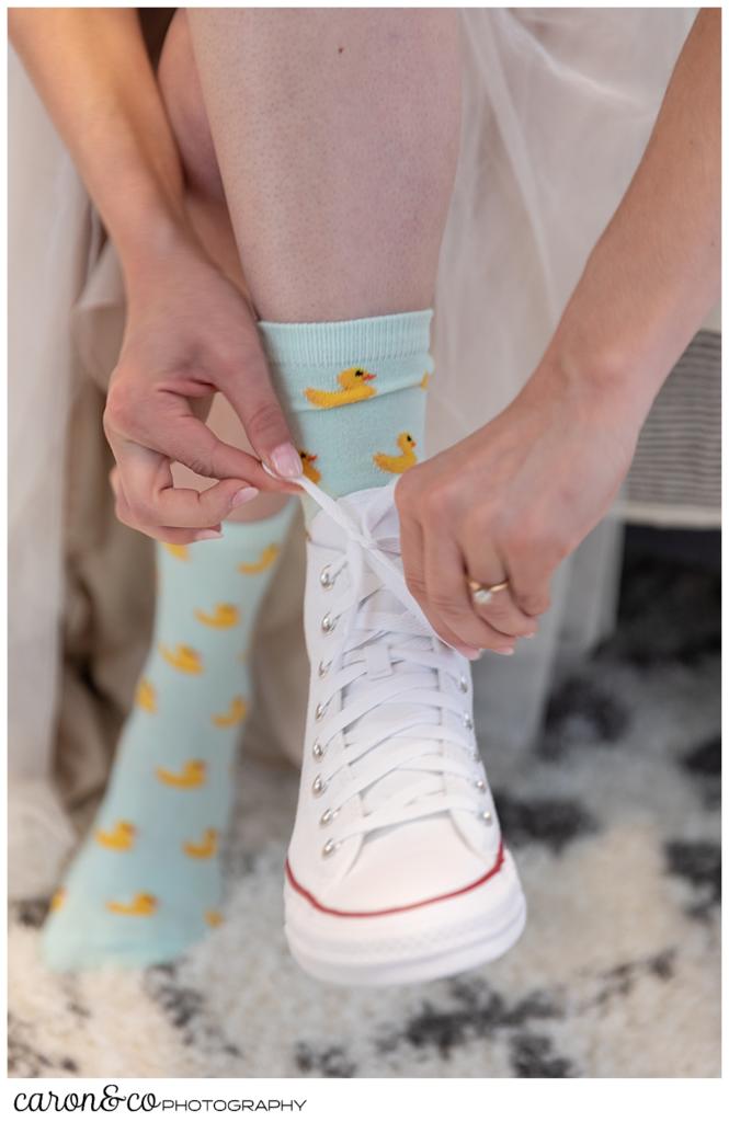 woman tying her converse shoes while wearing green socks with ducks