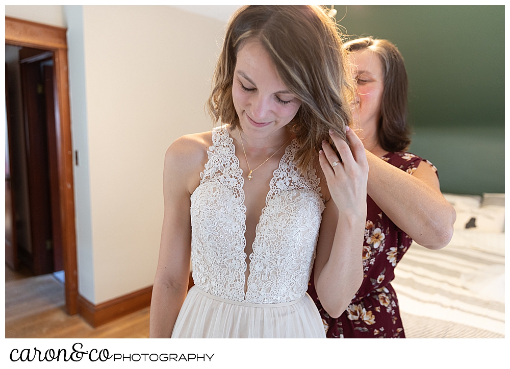 bride getting dressed as her mother helps with the zipper