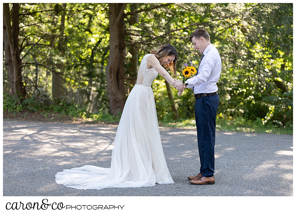 bride and groom stand facing each other looking at her beautiful wedding dress during their wedding day first look