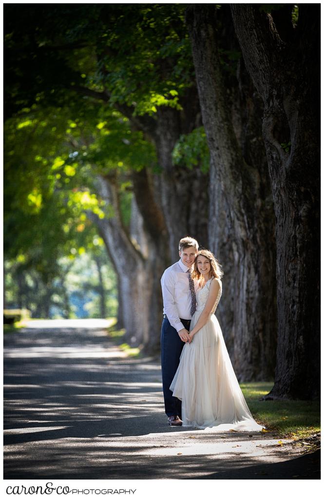 bride and groom standing in a road lines with tall trees