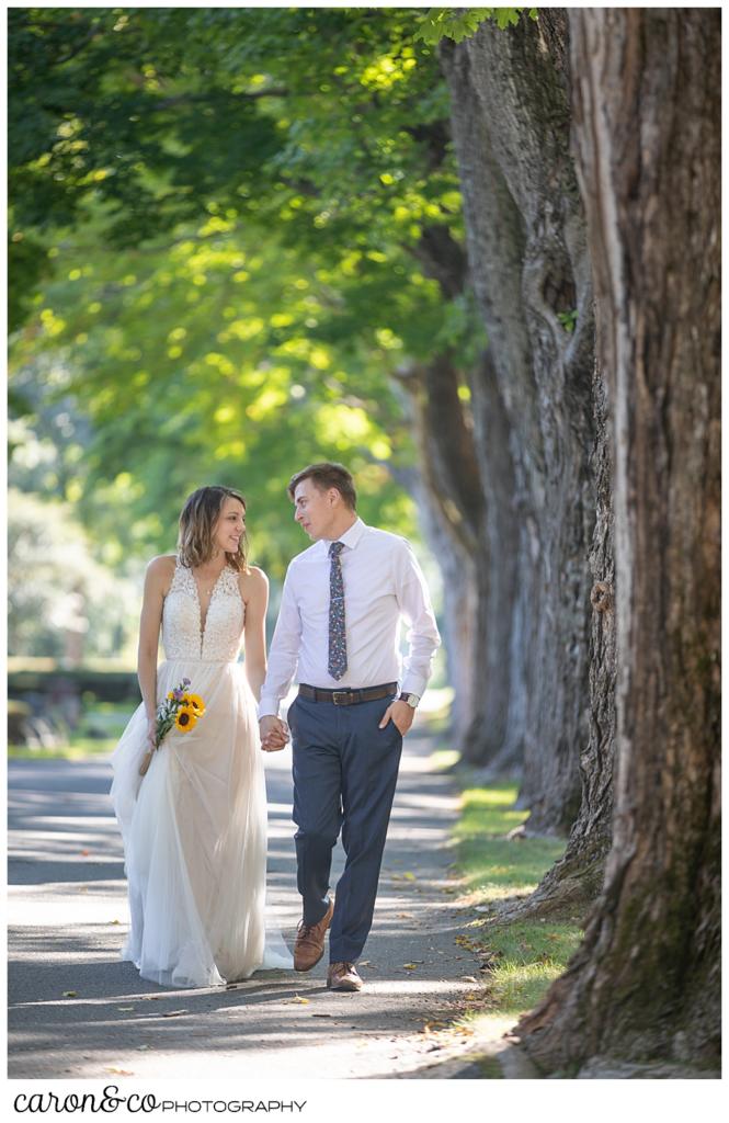 bride and groom walking along a road lined with tall trees