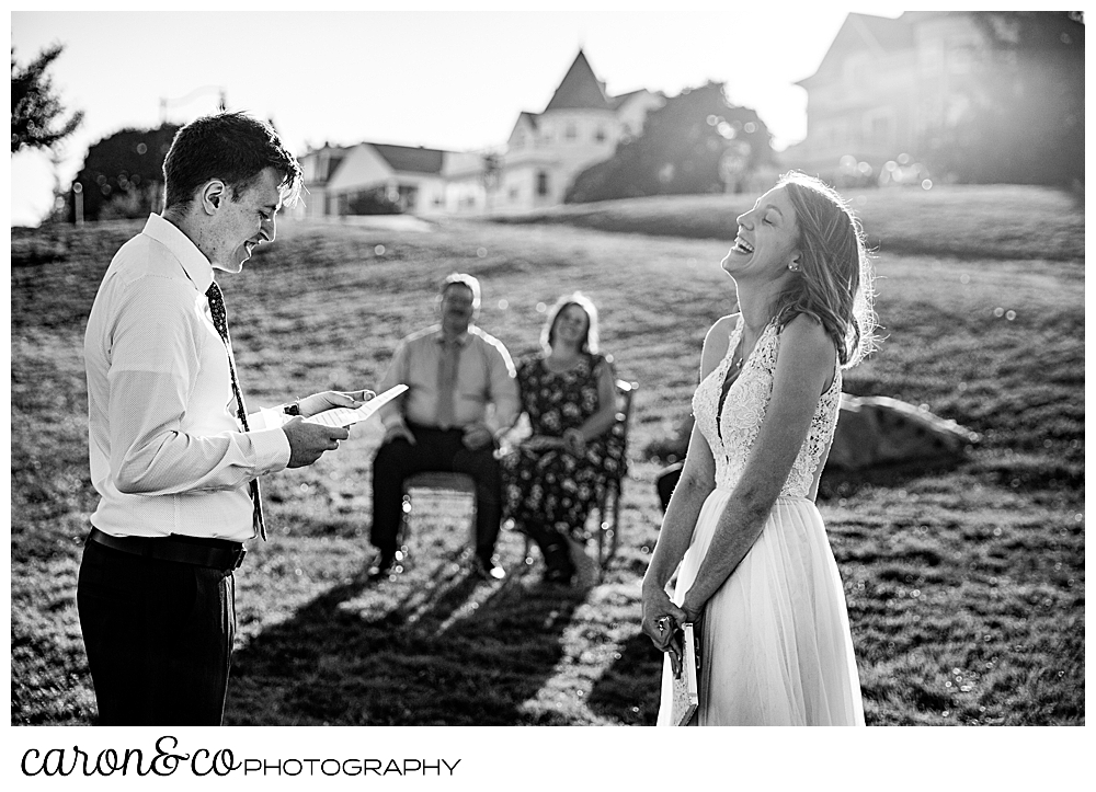 black and white photo of a bride and groom standing together, the groom is reading his vows, the bride's head is back and she is laughing during their sweet Portland Maine elopement