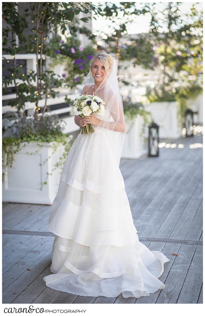 a full length portrait of abeautiful bride, wearing a strapless Carolina Herrara bridal gown and veil, and holding her bouquet