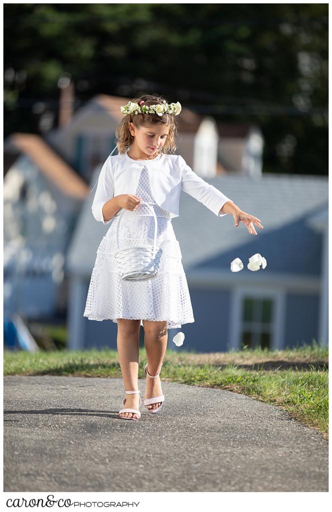 a lower girl, wearing a white dress and floral crown, drops flower petals during a timeless Boothbay Harbor wedding in Maine