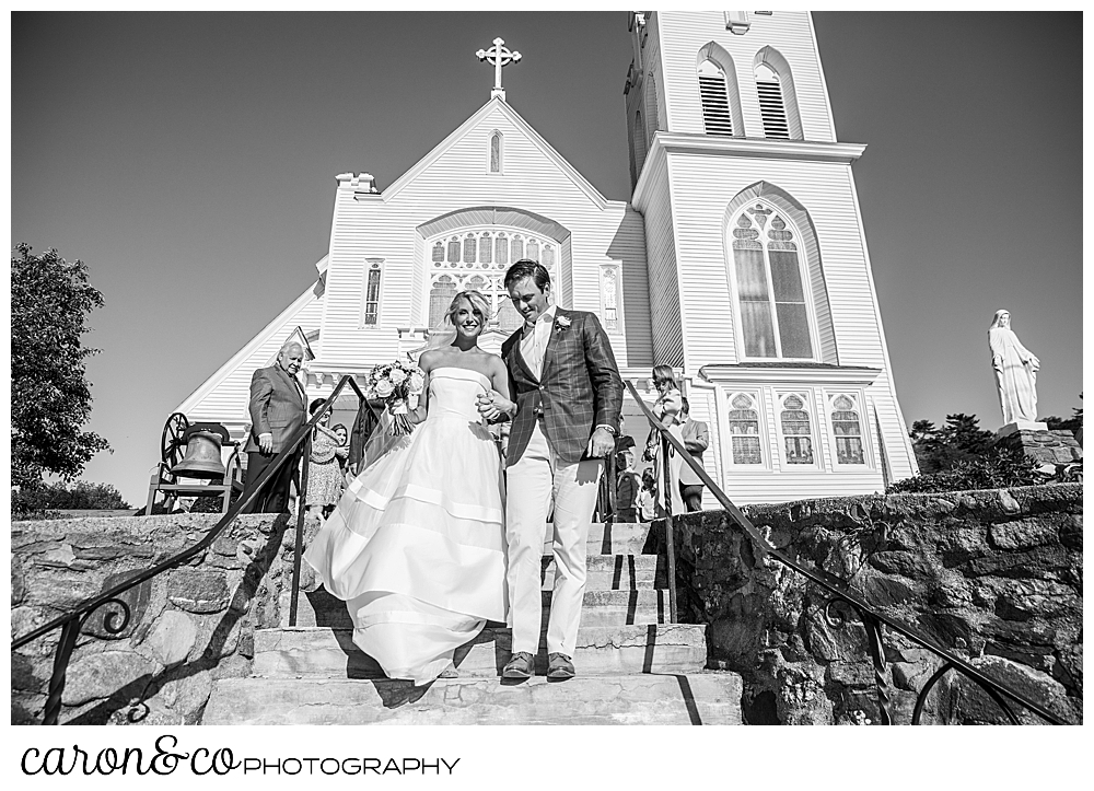 A black and white photo of a bride and groom walking down the steps at Our Lady Queen of Peace, timeless Boothbay harbor wedding