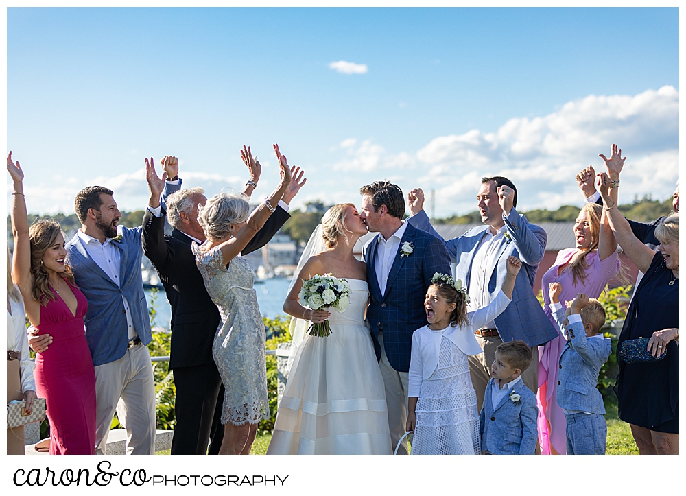 a bride and groom kiss, while their families cheer at their Boothbay Harbor, Maine wedding