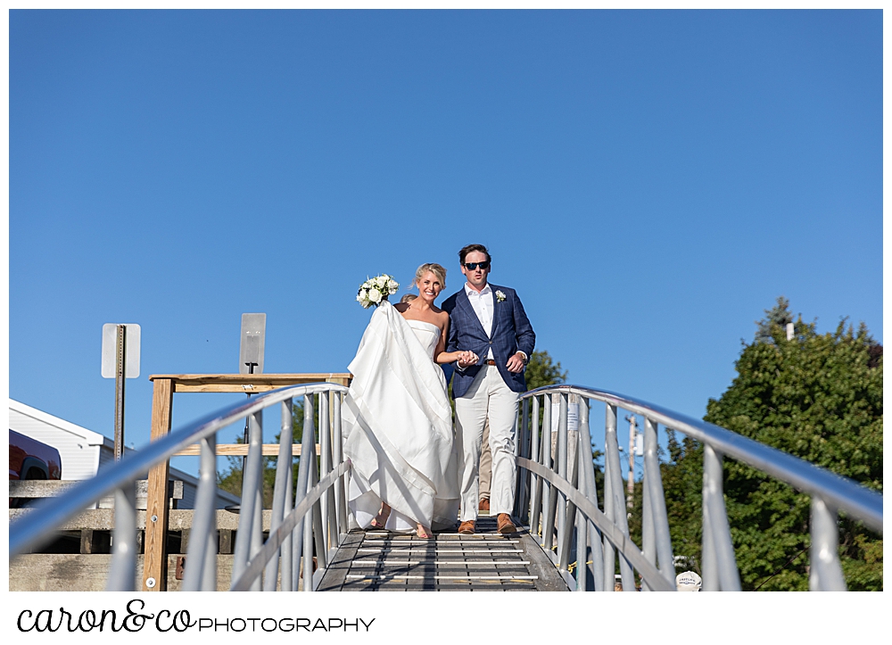 A bride and groom walk down a dock during their Boothbay Harbor, Maine wedding