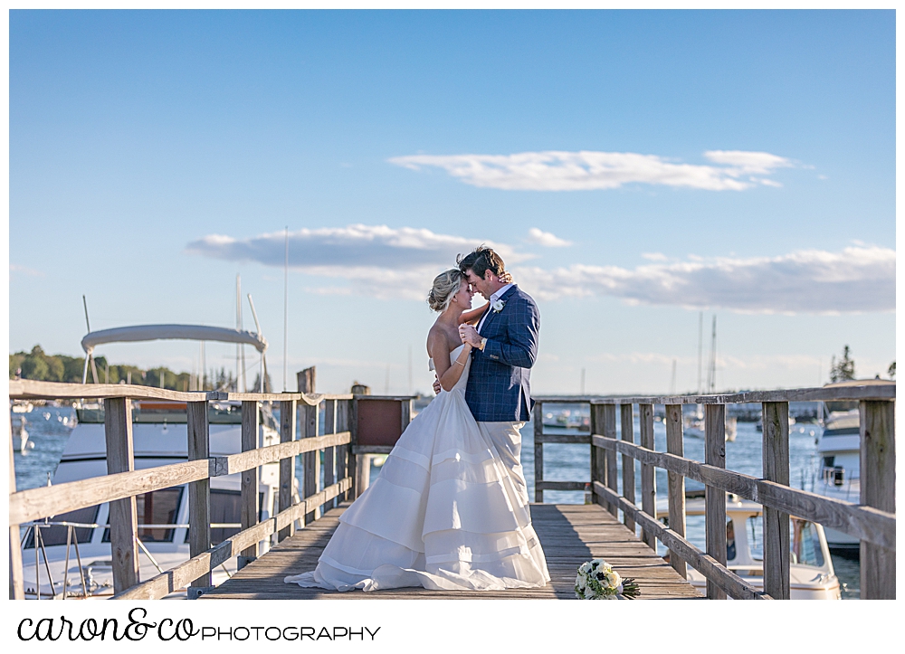 a bride and groom are dancing on a dock, their foreheads are touching, during their timeless Boothbay Harbor wedding