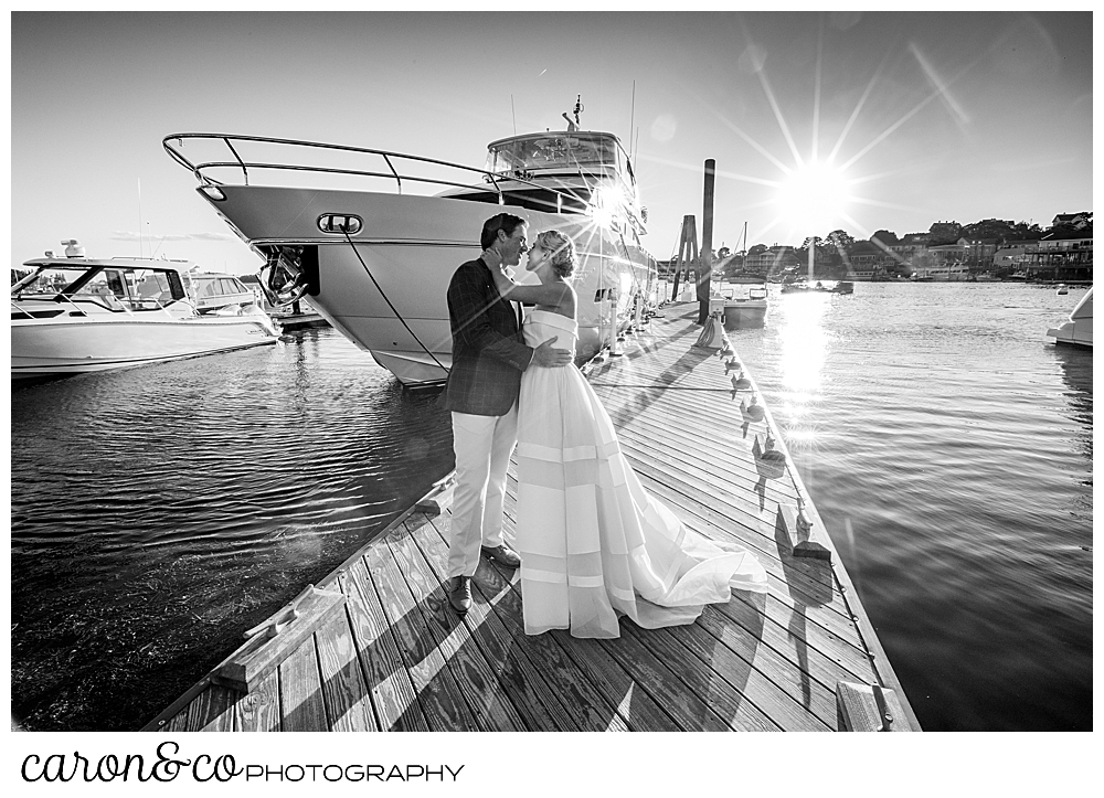 black and white photo of a bride and groom standing together on a dock, next to a motor yacht, during their timeless Boothbay Harbor wedding, Boothbay Harbor, Maine