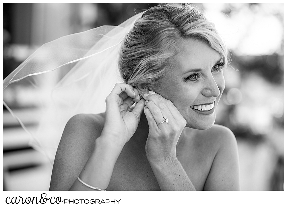 a bride wearing veil, and smiling, is putting on an earring