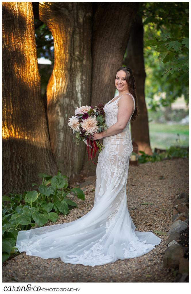 full length bridal portrait of a bride standing on a wooded path, holding a bouquet of blush and dark red dahlias