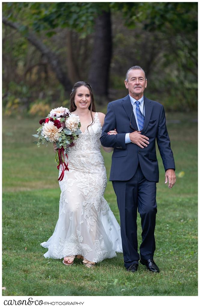 a bride and her father walk towards the ceremony site during a charming Kennebunkport Maine wedding