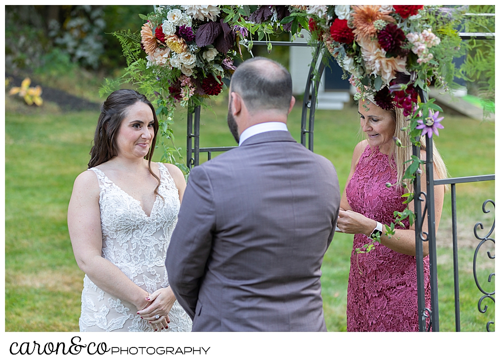 bride and groom standing in front of an arbor, during their wedding ceremony