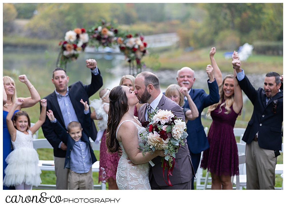 a bride and groom kiss, while their guests cheer behind them at a charming Kennebunkport Maine wedding ceremony