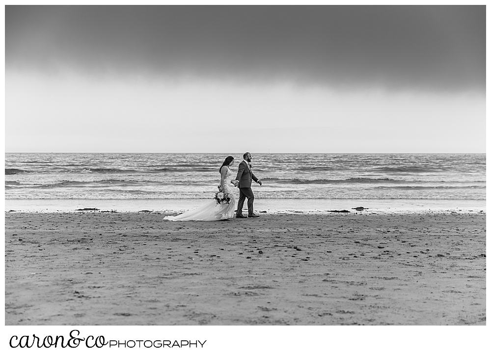 black and white photo of a bride and groom walk along the water's edge in Kennebunk Maine