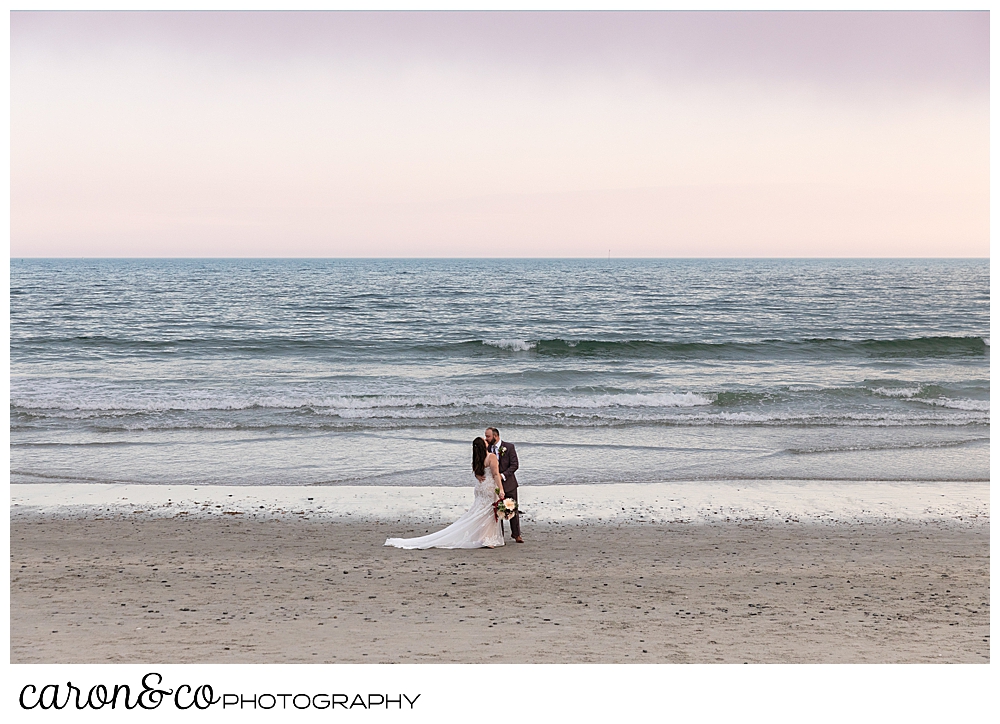 a bride and groom kiss at the water's edge, in Kennebunk Maine