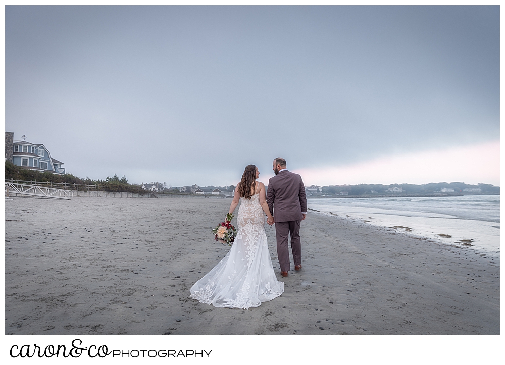 a bride and groom walk along the water at a Kennebunk Maine beach