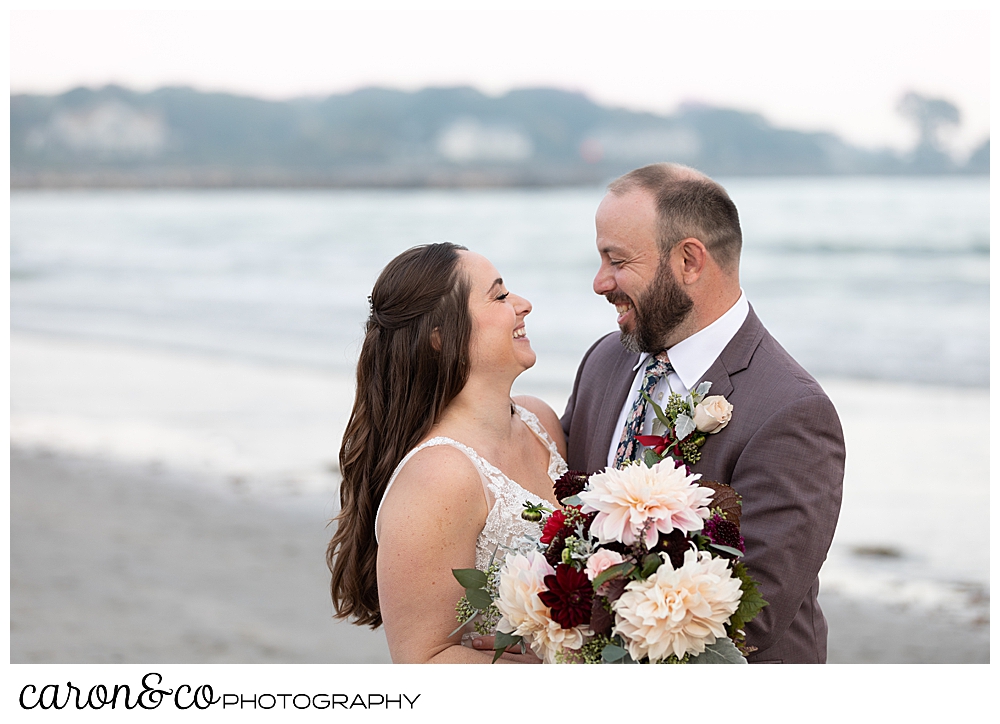 a bride and groom standing together and smiling at each other at a Kennebunk Maine Beach