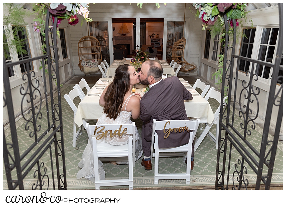 a bride and groom kiss while sitting at their charming Kennebunkport maine wedding reception