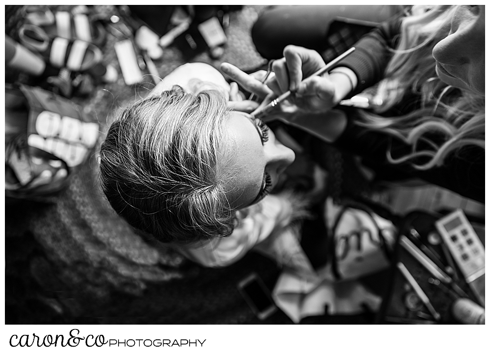 black and white photo of a makeup artist applying makeup on a bride, from an overhead perspective 