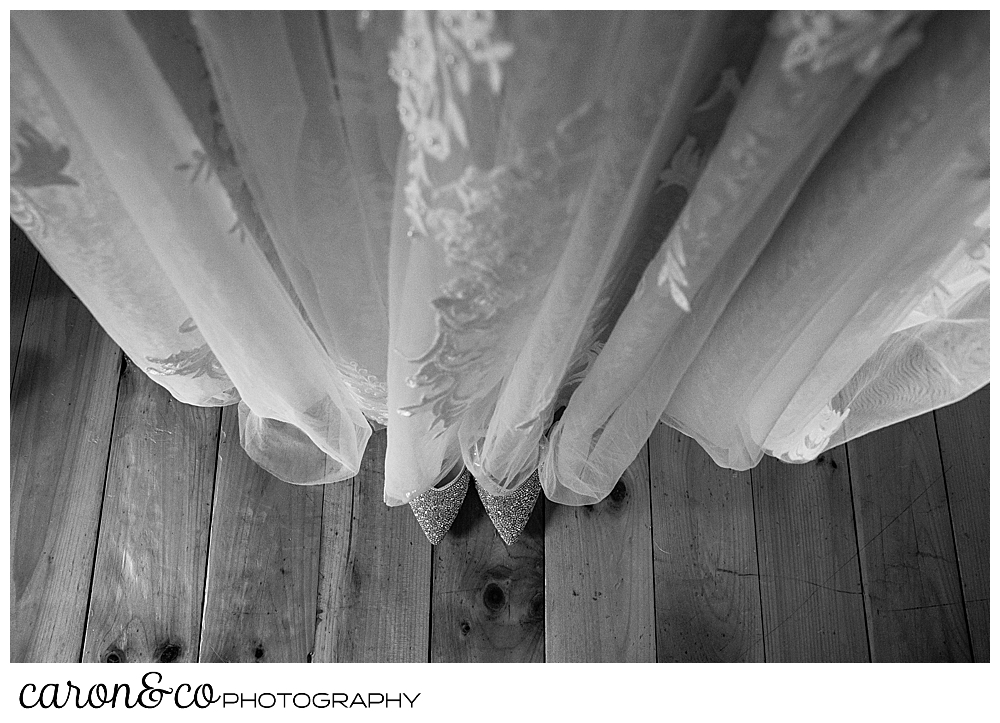 black and white photo of the skirt of a wedding dress, with a pair of sparkly shoes peeking out from below