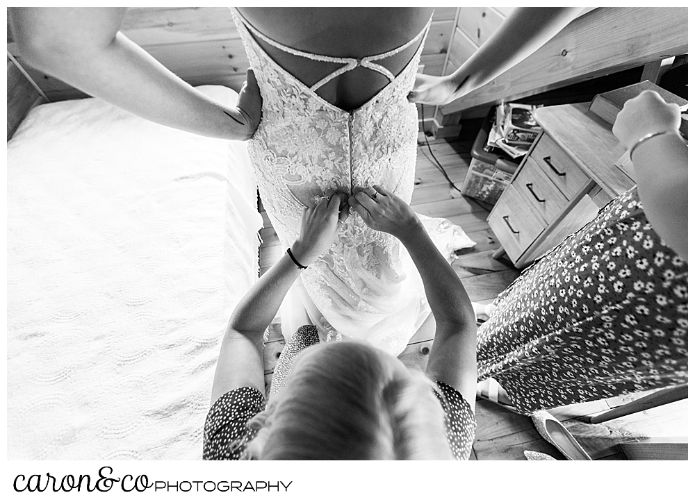 black and white image of a bride having her dress buttoned in the back